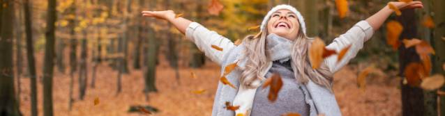Frau wirft freudig Blätter in die Luft und steht im farbigen Herbst-Wald